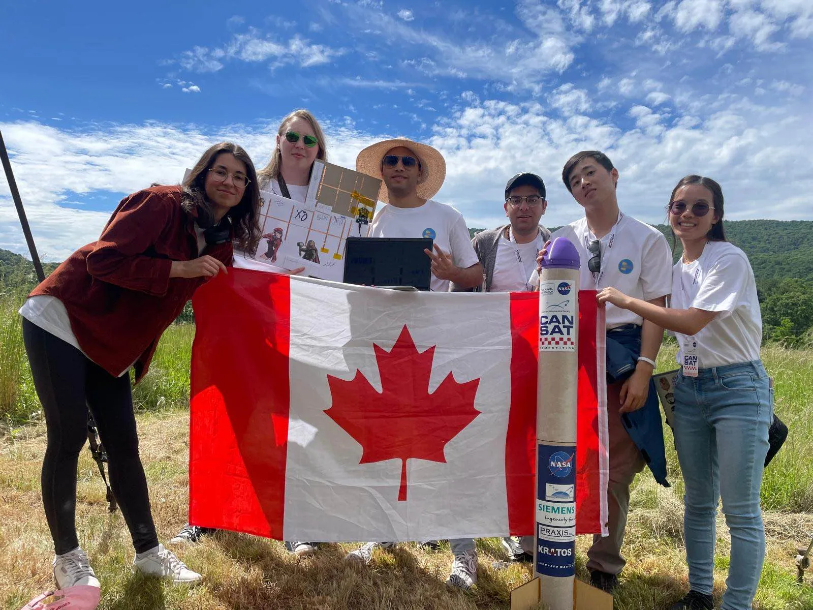 TMU CanSat team members holding a Canadian flag beside their CanSat rocket