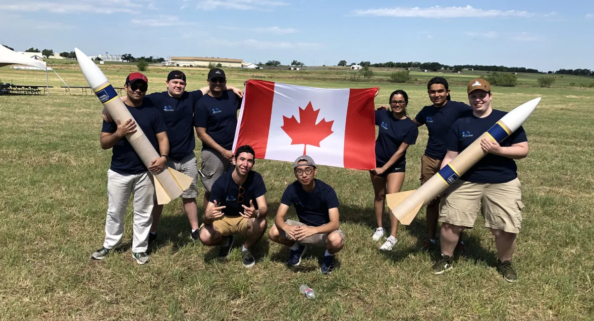 CanSat team members holding two rockets and a Canadian flag